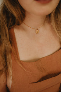 Delicate gold necklace with Saraswati stamped into circle pendant on model.